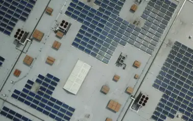 Aerial view of a flat roof densely covered with rows of solar panels and scattered rooftop equipment.