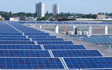 Rooftop row after row of blue solar panels on a flat building roof with a city skyline in the distance on a clear day.